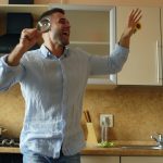 Attractive young funny man dancing and singing with ladle while cooking breakfast in the kitchen at home in the morining